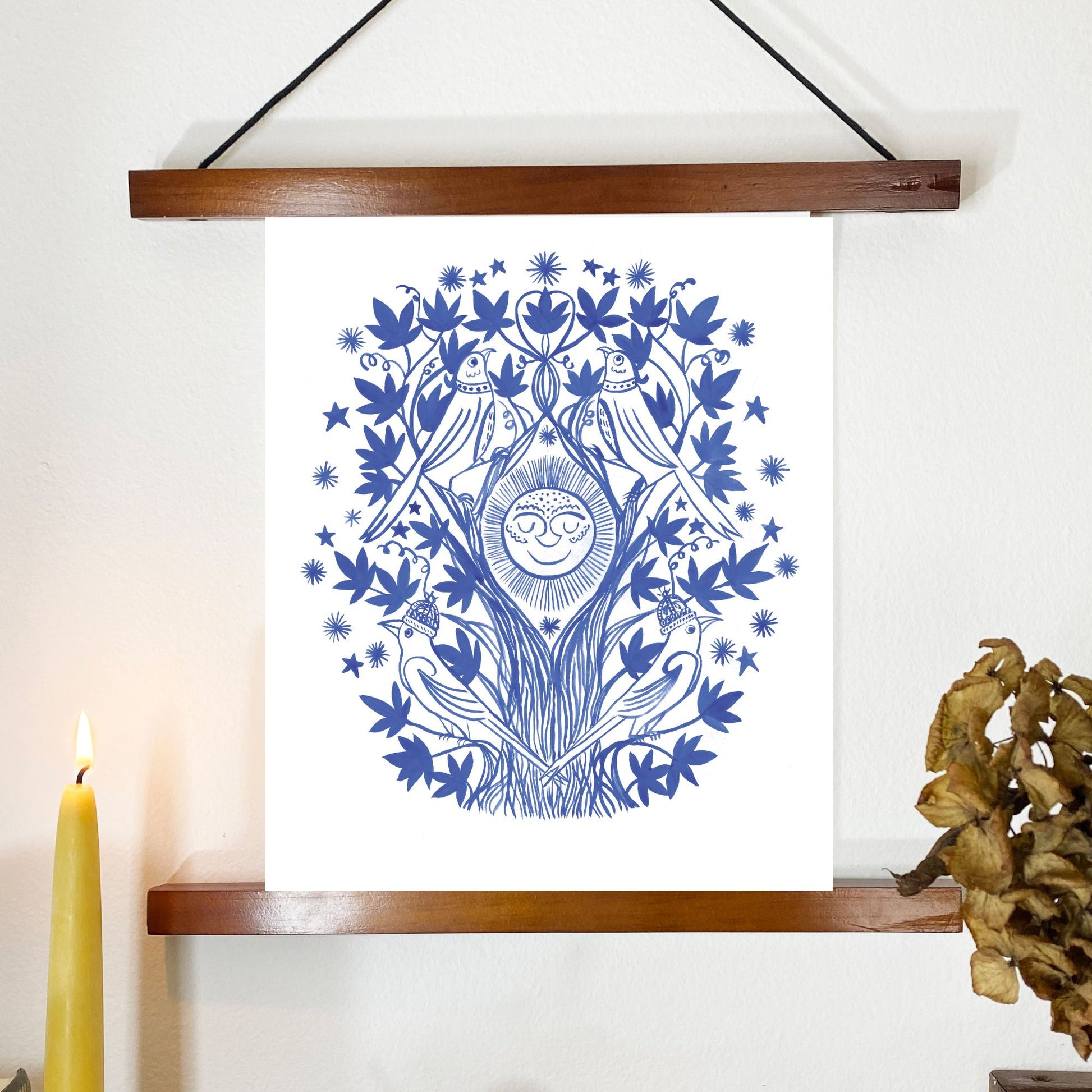 Framed artwork with blue tree design on a white background, candle and decorative object on the side.