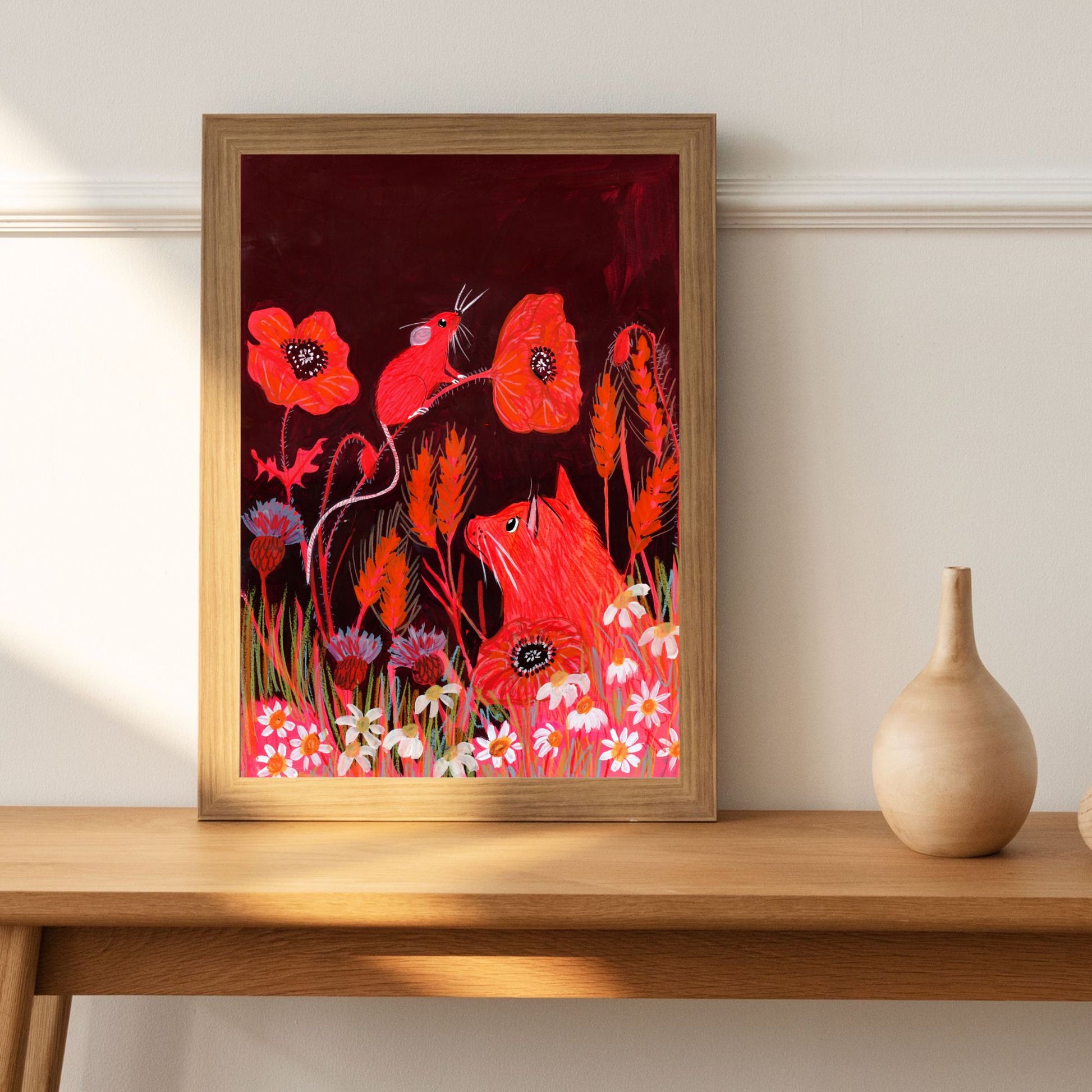 Framed artwork of red foxes and flowers on a wooden table.