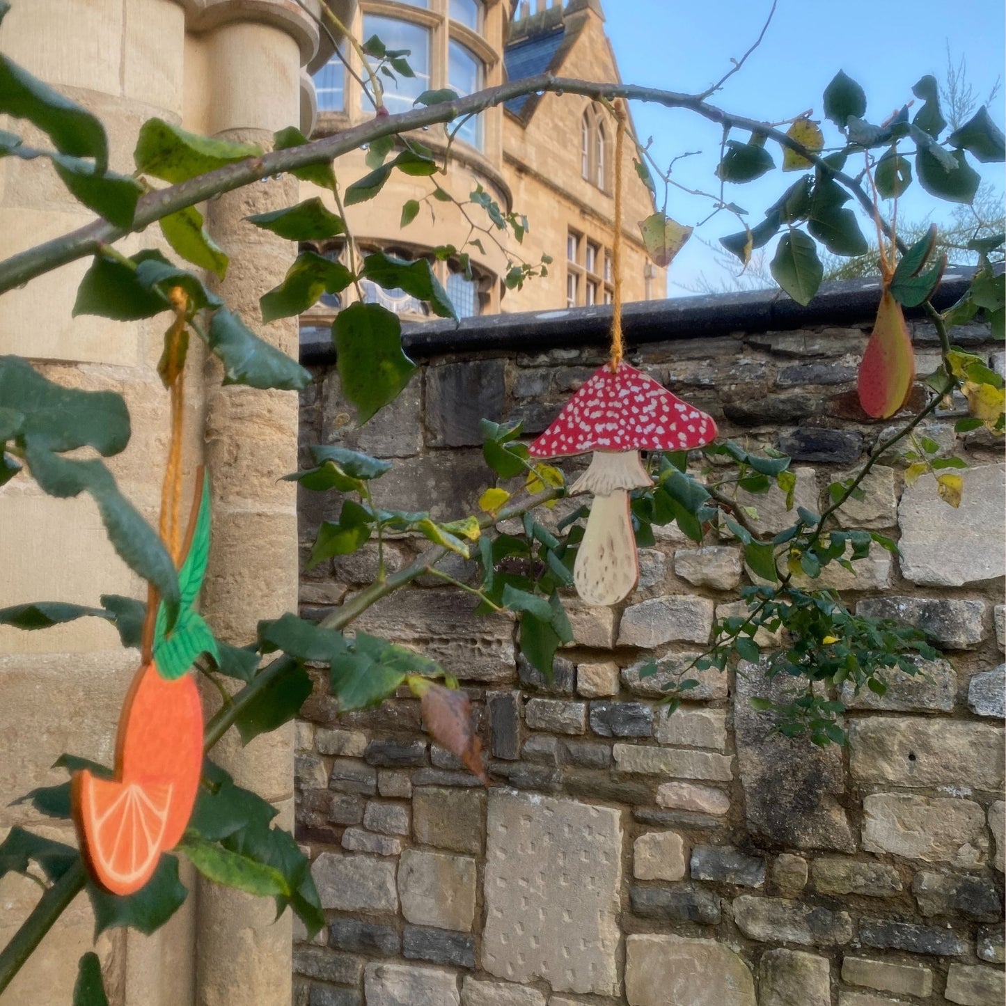 Decorative items hanging from a tree branch in front of a stone building.