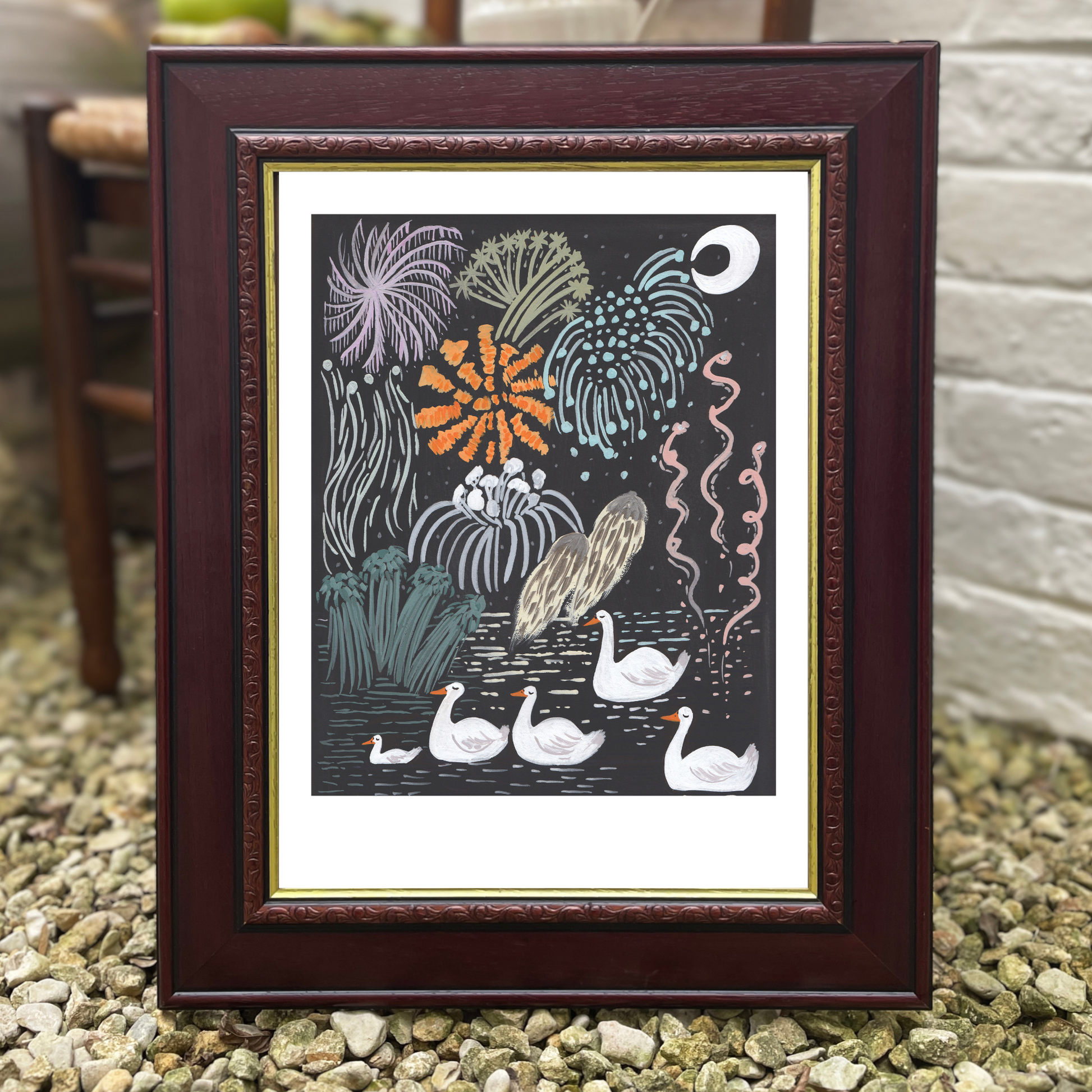 Framed artwork with swans and plants on a pebbled surface