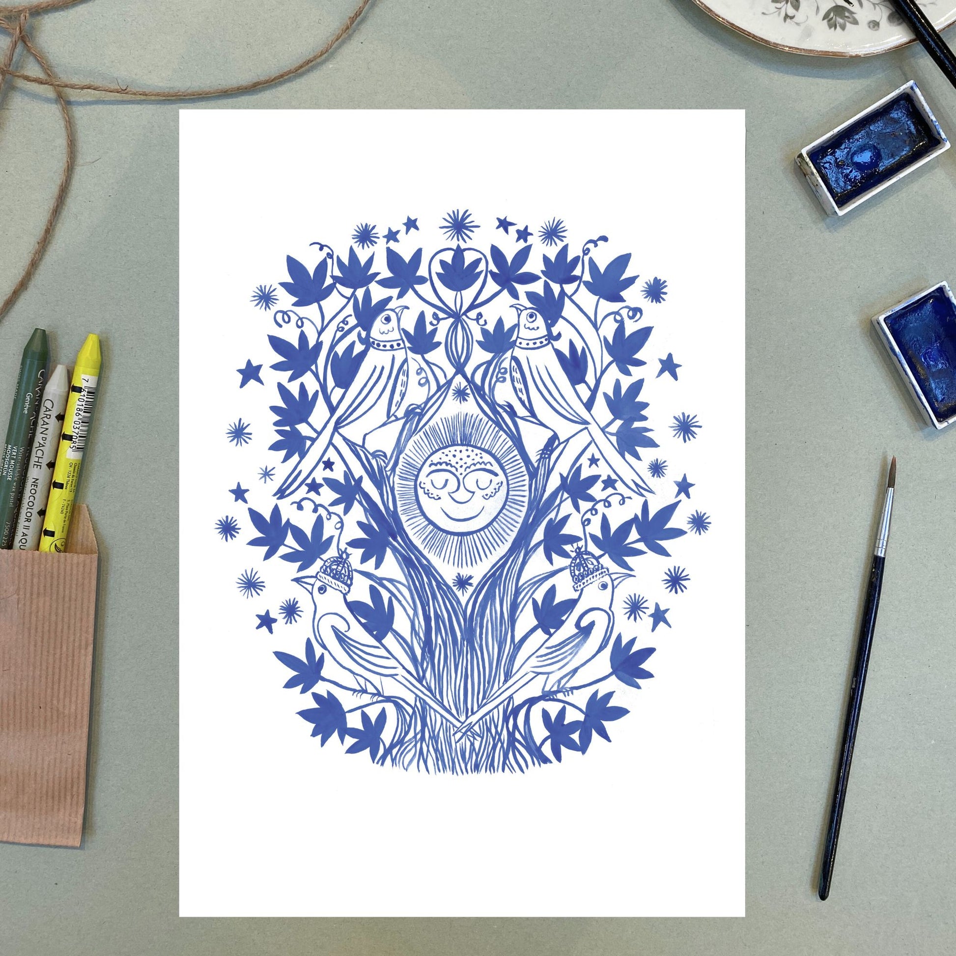 Blue floral and bird illustration on a white background with art supplies around.