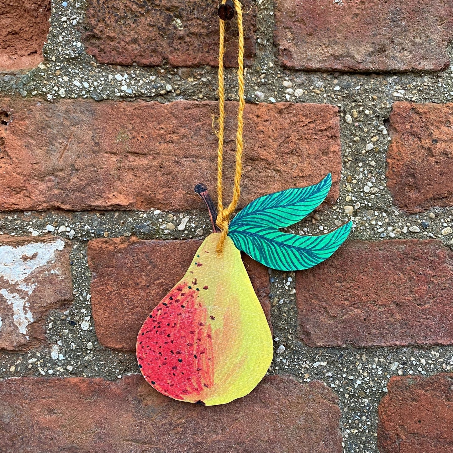 Colorful pear-shaped ornament with leaves hanging on a brick wall.