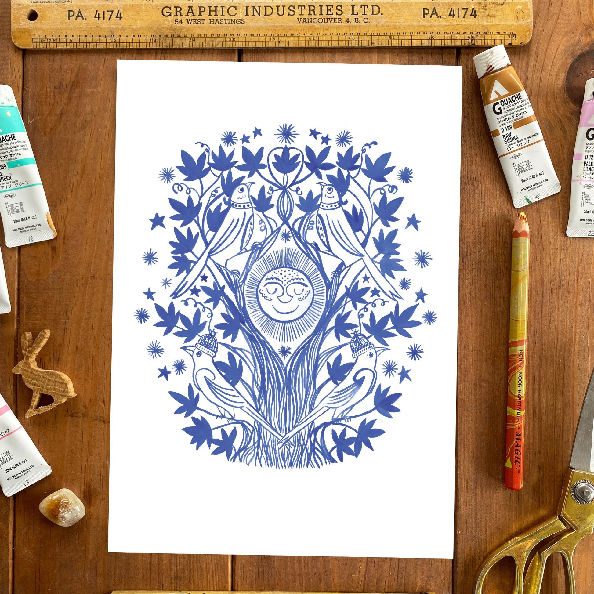 Artistic blue design on white paper with art supplies on a wooden surface