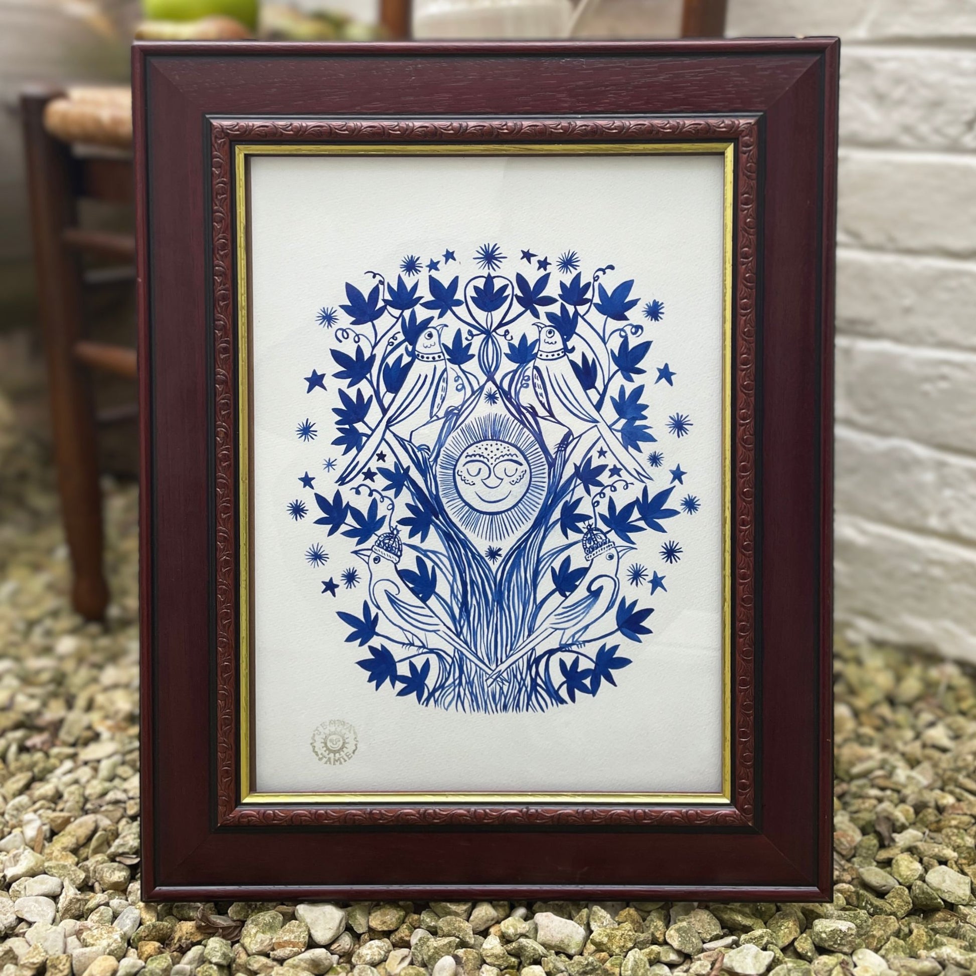 Framed artwork with blue tree design on a white background, placed outdoors.