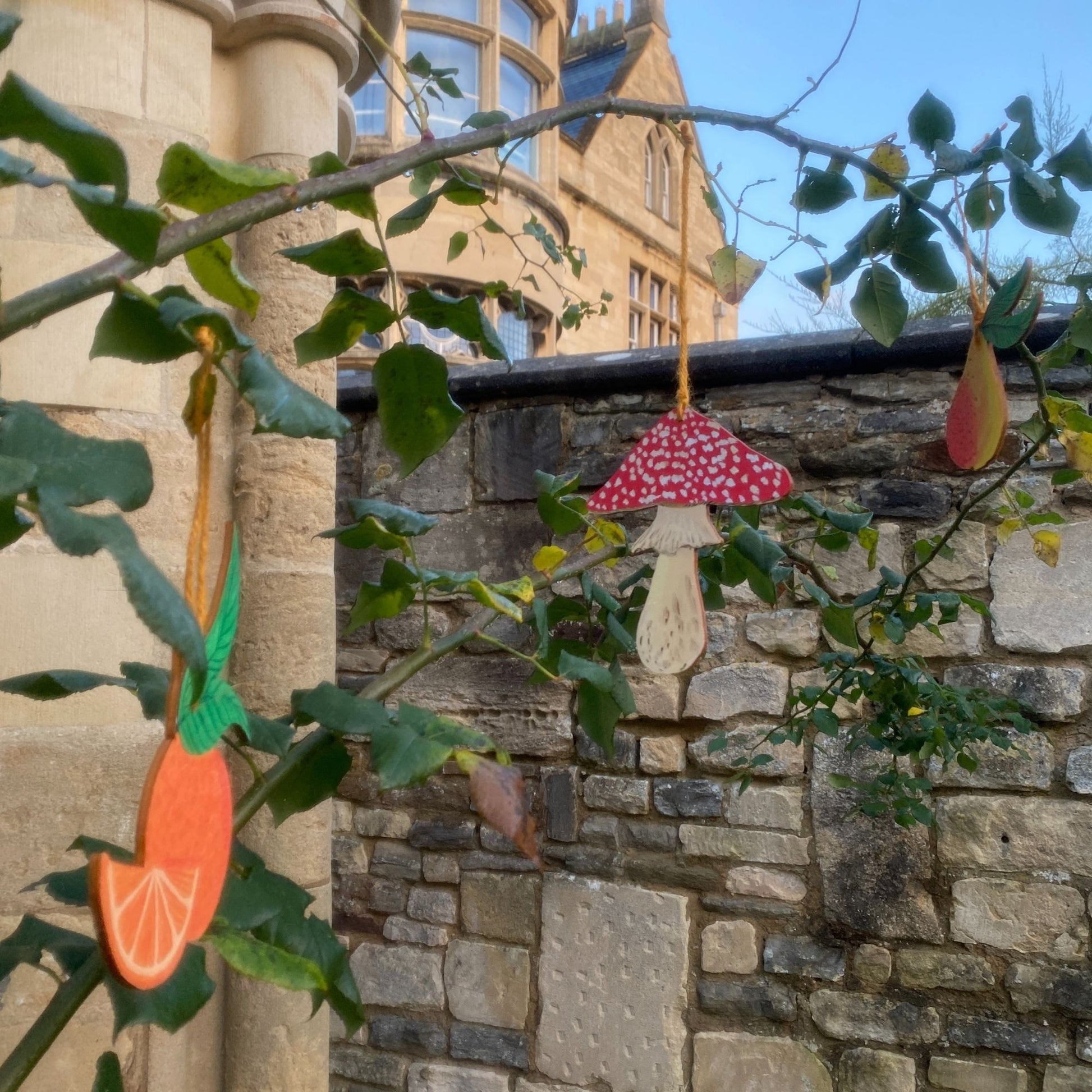 Decorative hanging items on a tree branch with a stone building in the background