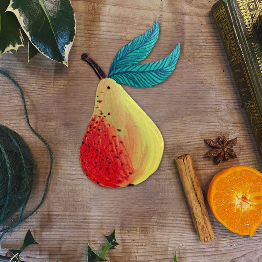 Colorful pear-shaped fruit decoration on a wooden surface with leaves, cinnamon stick, and orange.