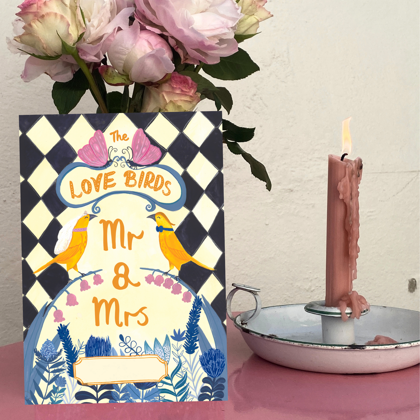 Card with 'Love Birds Mr & Mrs' design, pink candle, and flowers on a checkered background
