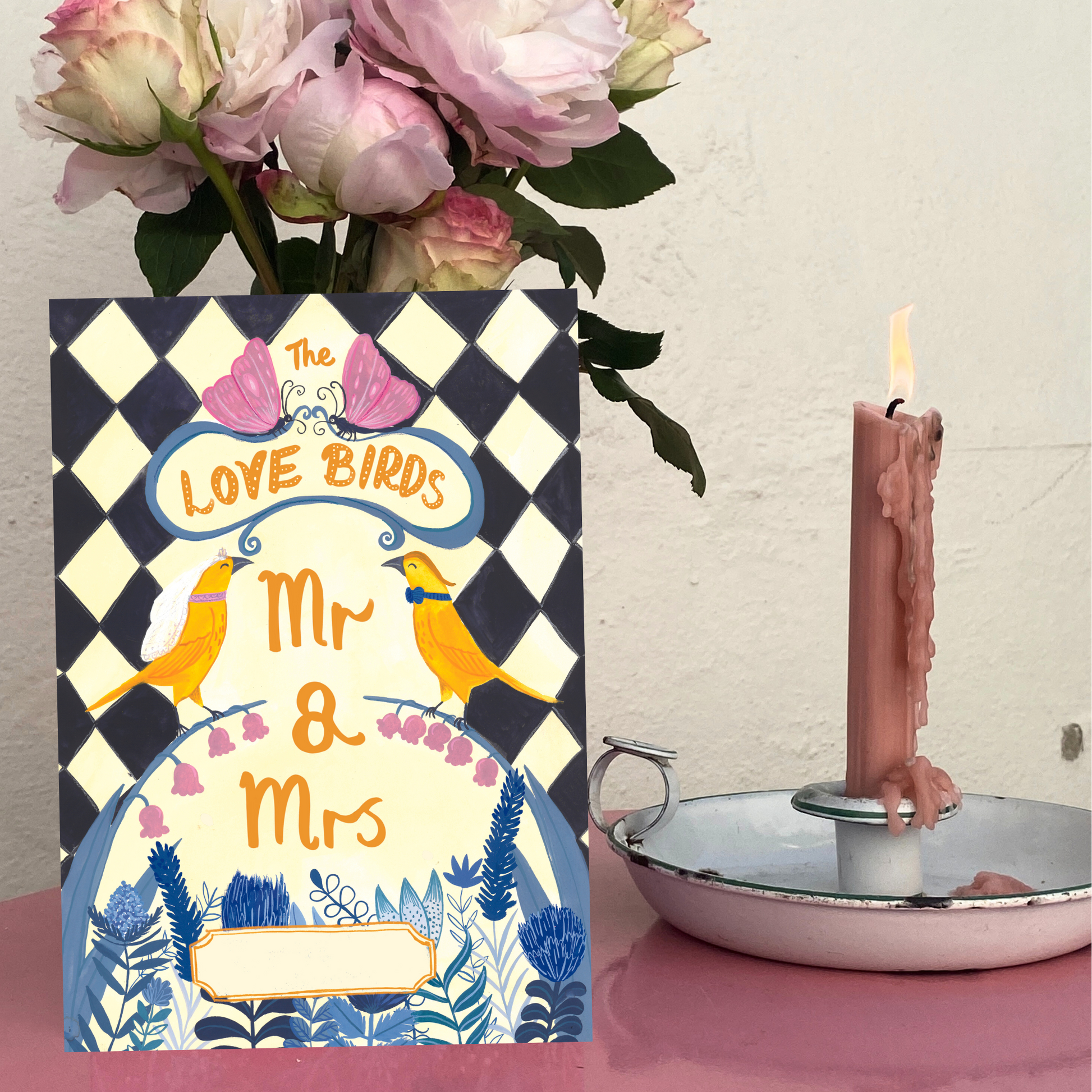 Card with 'Love Birds Mr & Mrs' design, pink candle, and flowers on a checkered background