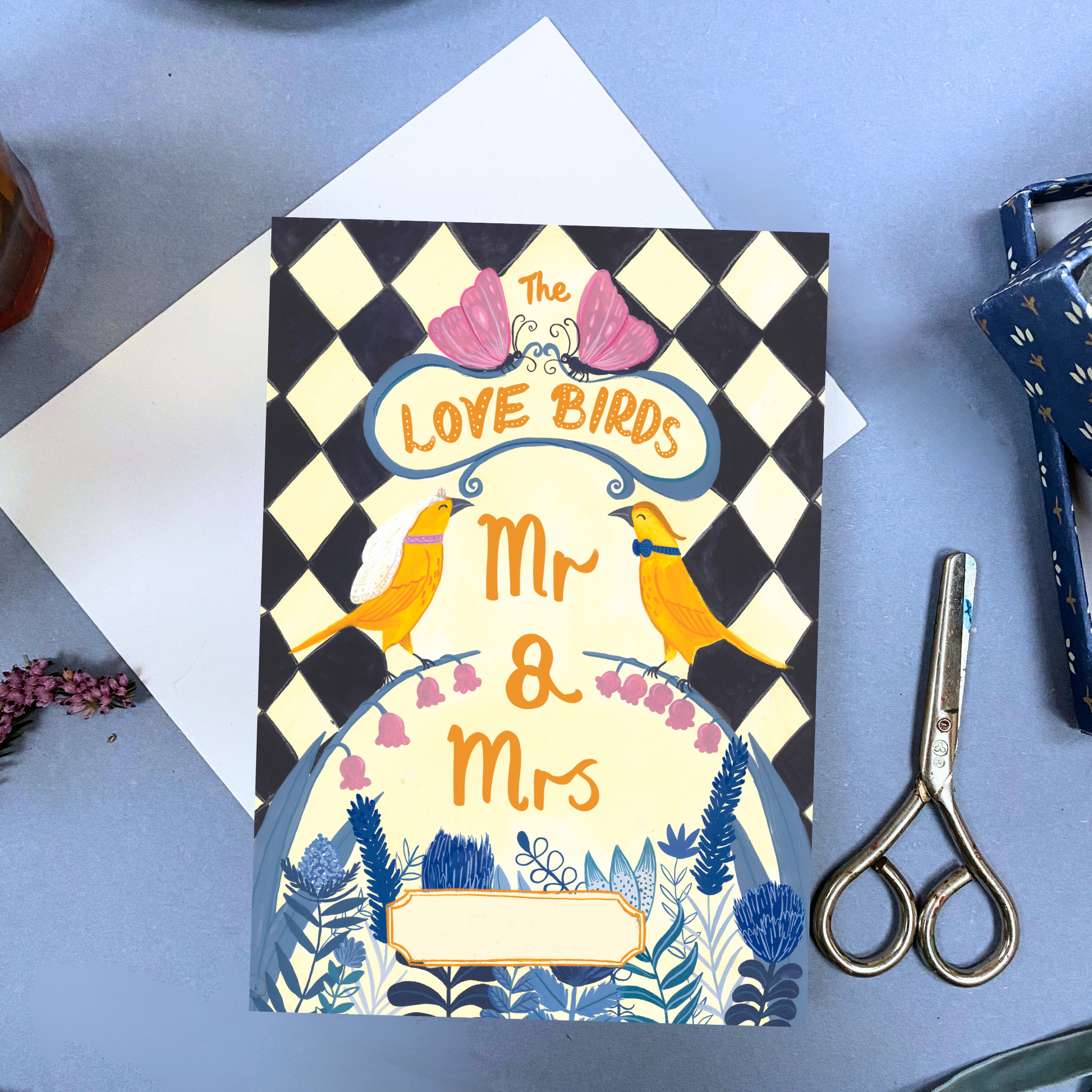 Greeting card with 'Mr & Mrs' text and checkered design on a blue surface with scissors.