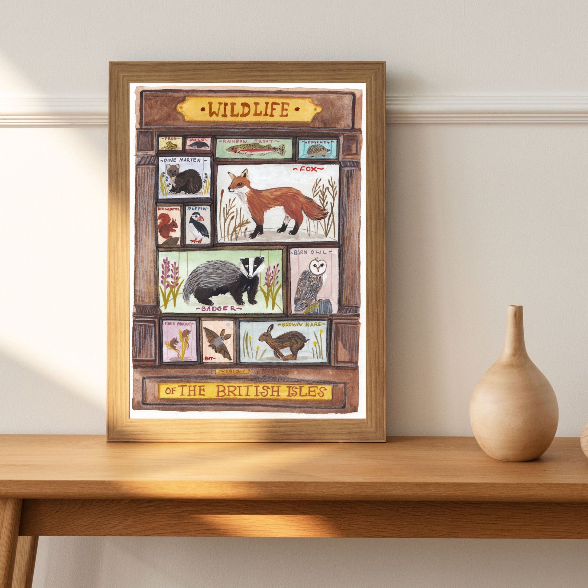 Framed artwork of British wildlife on a wooden table with a vase.